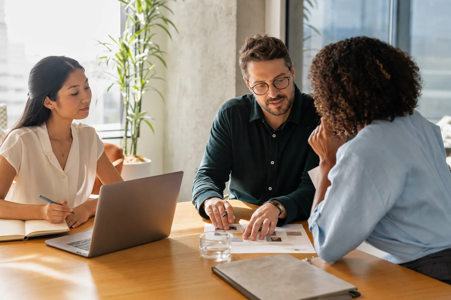 A consultant walks a client through a printed proposal at a bright meeting table while a colleague takes notes.